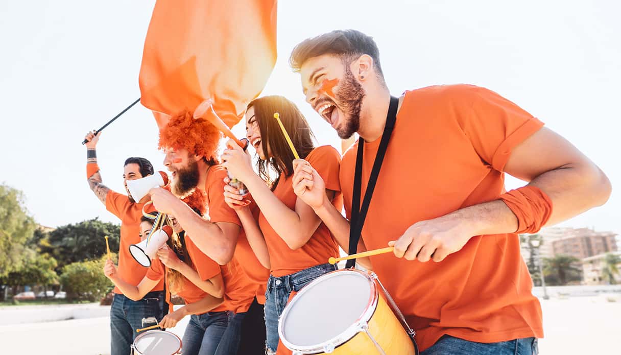 Groep mensen zijn aan het juichen voor het Nederlands elftal tijdens het EK voetbal 2024 met schmink op hun gezicht.
