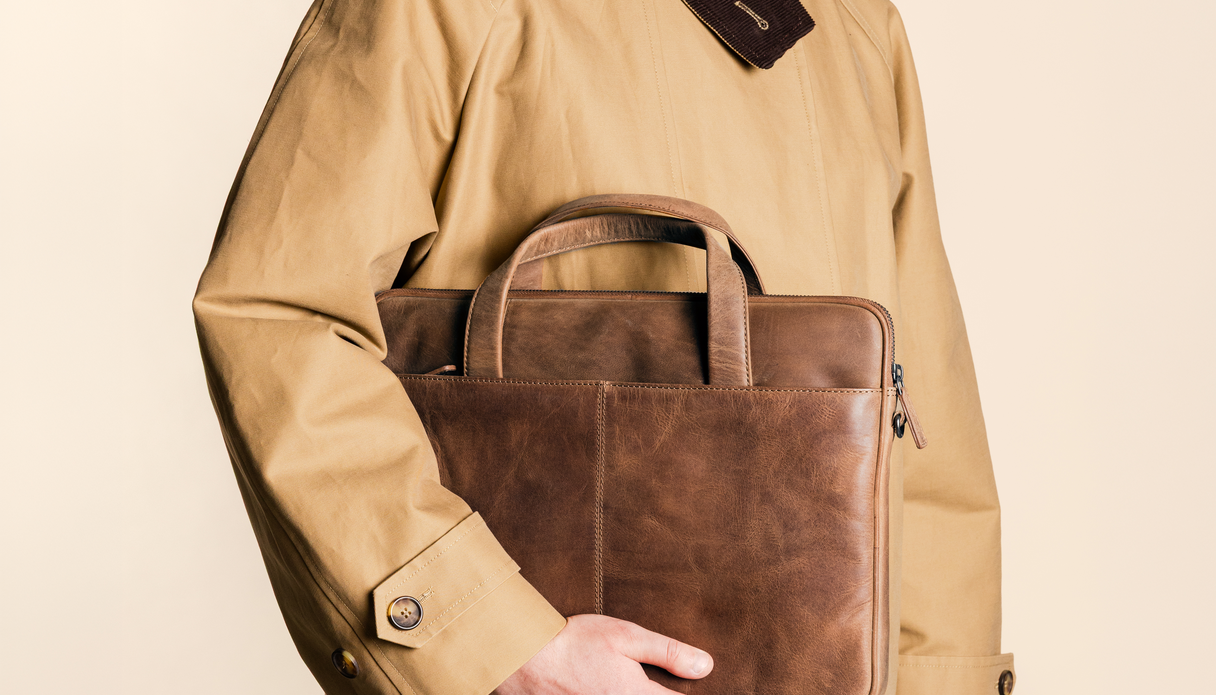 Een man houdt een lederen cognac kleurige laptop hoes voor zich vast.
