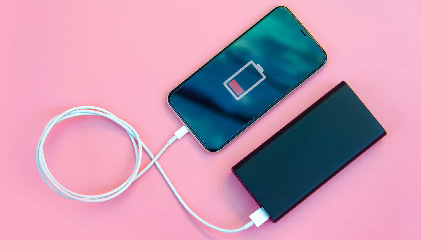 Flatlay op roze achtergrond van smartphone die door een powerbank wordt opgeladen.