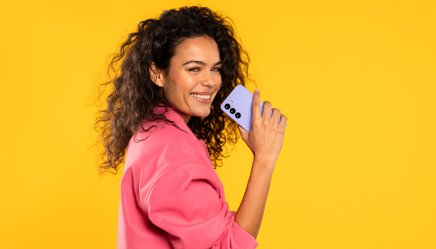 Vrouw houdt lachend paars telefoonhoesje vast, de achtergrond is geel.