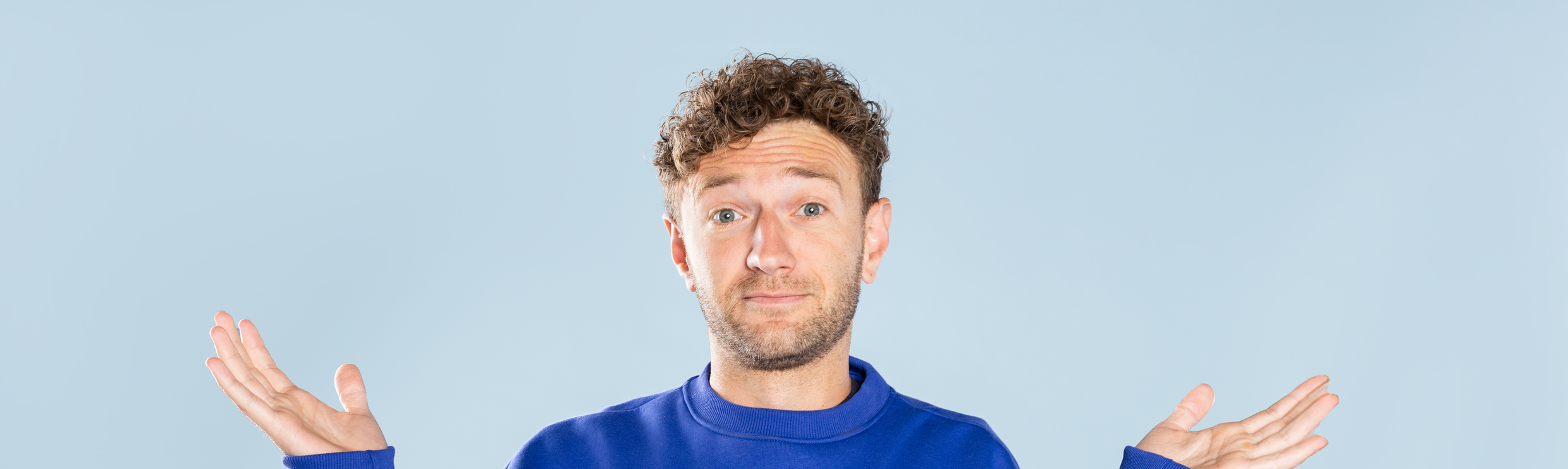 Een man die zijn armen omhoog houdt, alsof hij een vraag stelt of iets niet helemaal begrijpt.