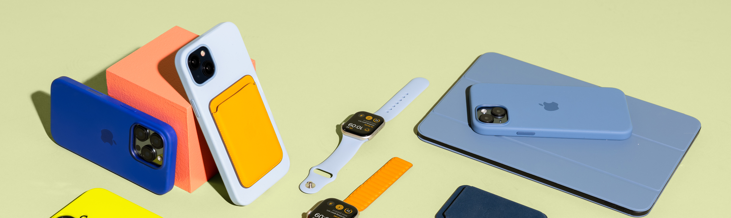 5 Apple iPhone's met kleurrijke Apple hoesjes, twee Apple Watches met kleurrijke bandjes en een Apple iPad.