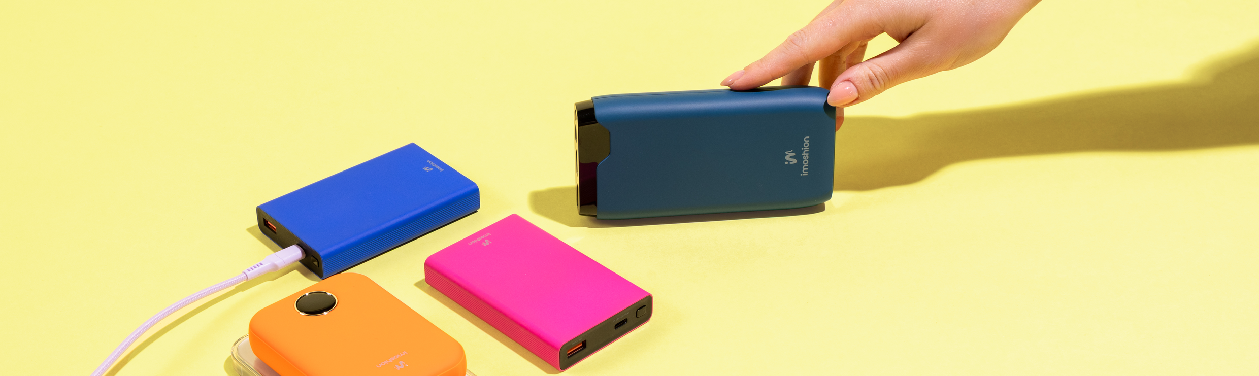 4 verschillende kleurrijke powerbanks, waarvan 1 MagSafe powerbank die aan een iPhone gekoppeld is, met een reikende hand naar een van de powerbanks.