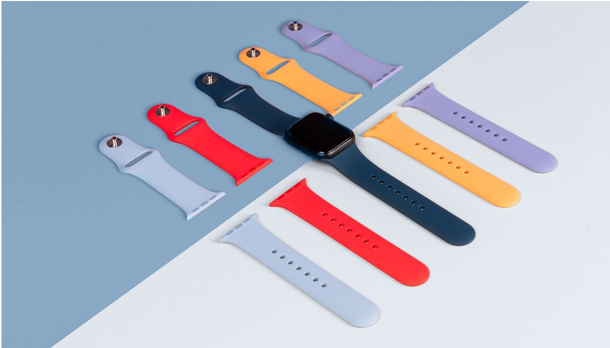 Je ziet een midnight-kleurige Apple Watch met een donkerblauw bandje. Andere bandjes liggen ernaast gestileerd uitgelijnd in verschillende kleuren. De ondergrond is half blauw, half wit.