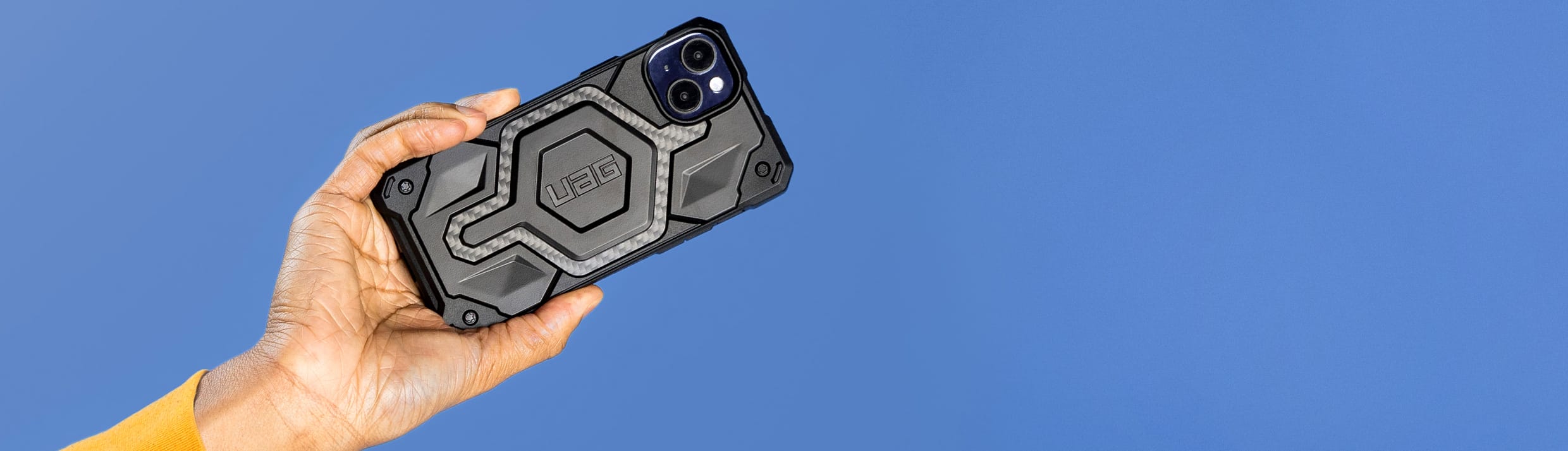 Een hand houdt een telefoon met een zwart UAG hoesje vast.