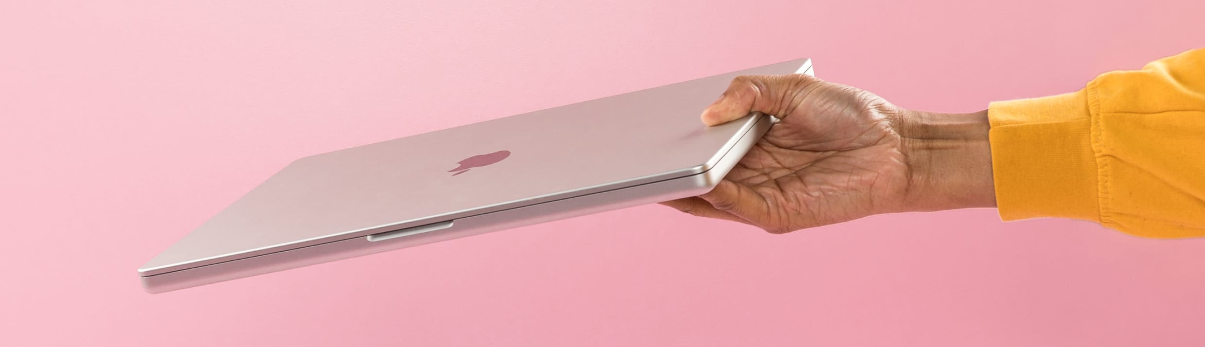 Een hand komt van rechts en heeft een MacBook vast.