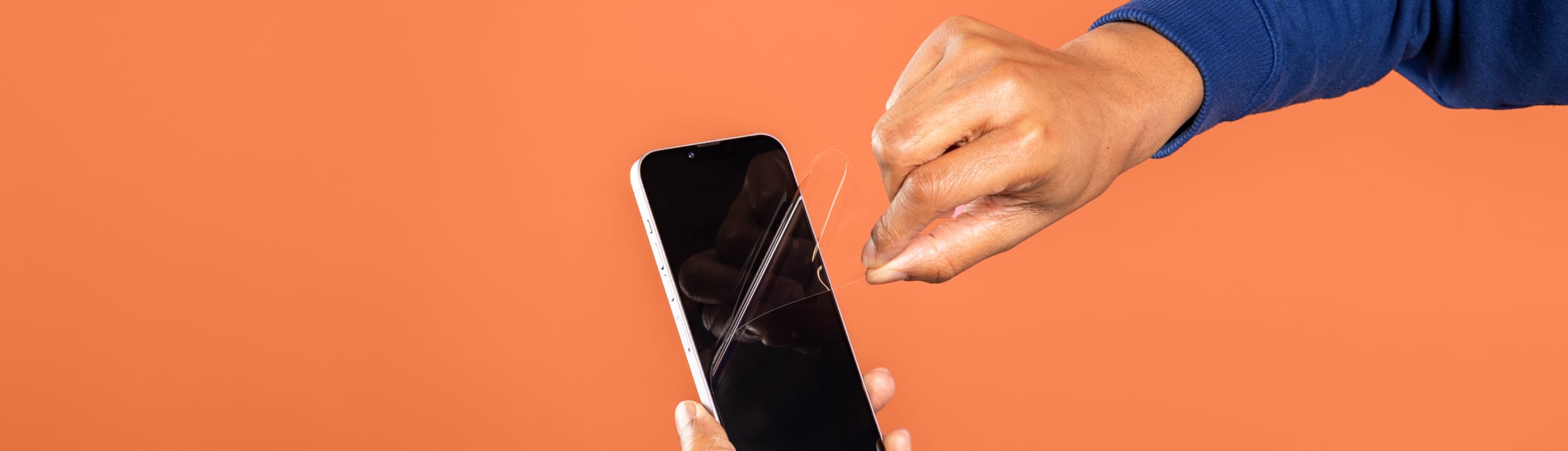 Je ziet een hand met een blauwe mauw een screenprotector verwijderen van een smartphone. De achtergrond is oranje.