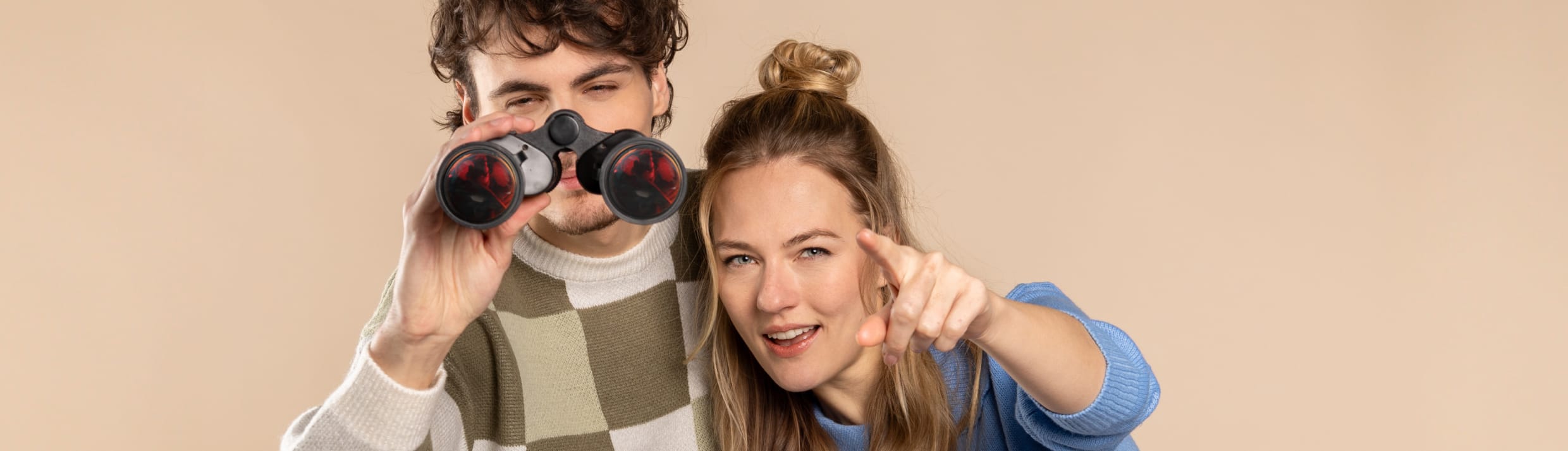 Een man met een verrekijker en een vrouw die in de verte wijst.