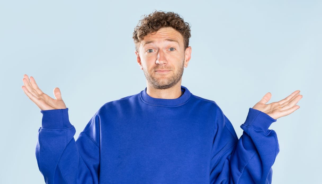 Een man in een kobalt blauwe trui steekt vragend zijn handen omhoog.