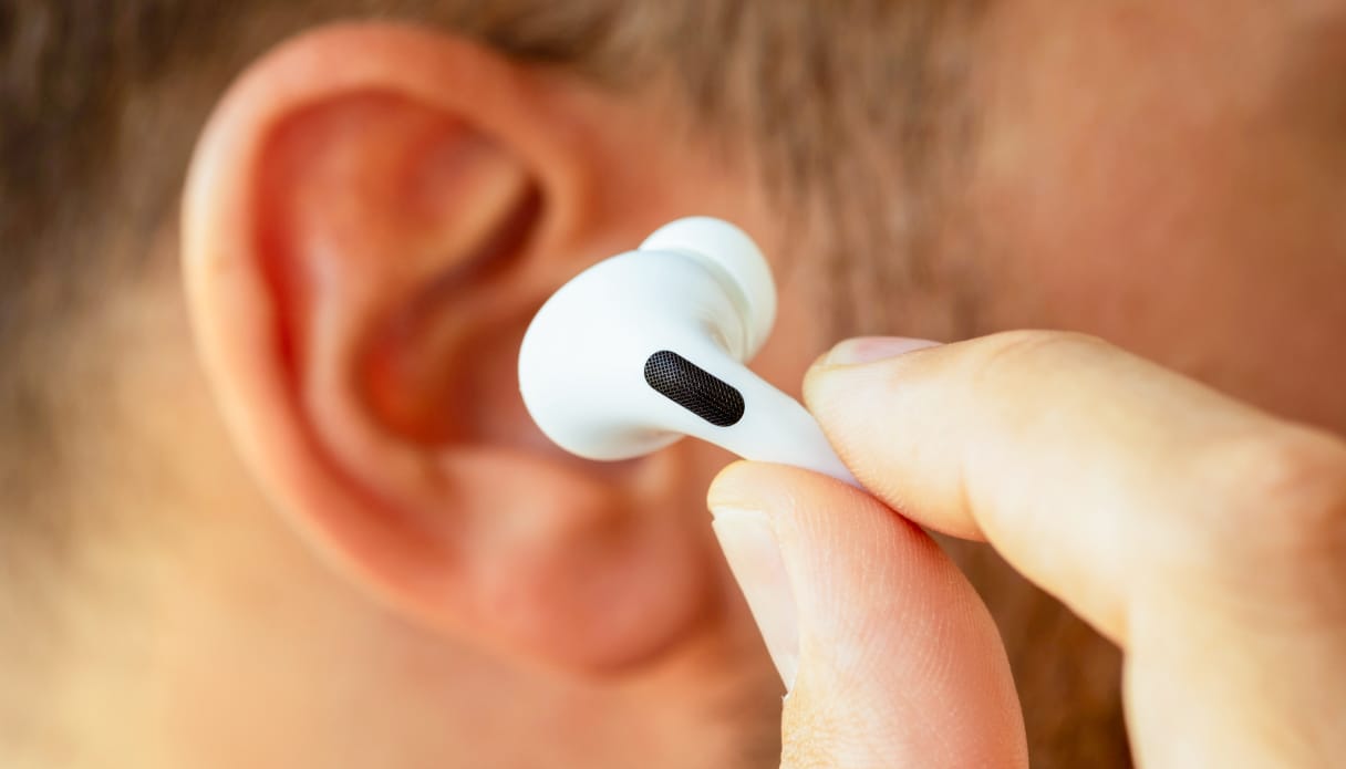 Je ziet een ingezoomd zijaanzicht van een mannenhoofd en zijn oor met donkerkleurig haar en lichte huidskleur. Hij houdt een Apple AirPod Pro voor zijn oren, deze is in focus en zijn oor is wat onscherp.