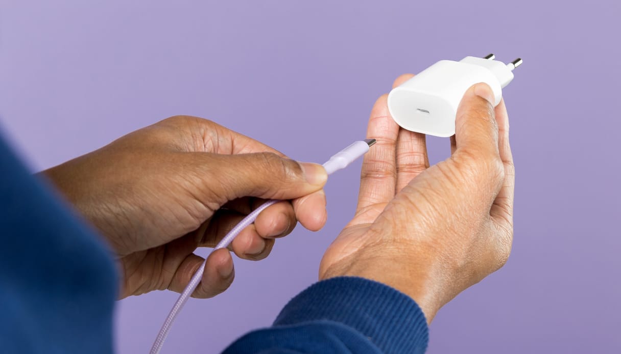Een hand die een USB-C oplaadkabel in een adapter steekt.