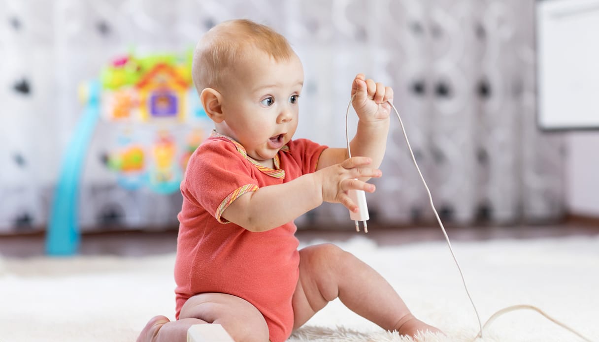 Een baby heeft een oplader in de hand en kijkt verbaast.