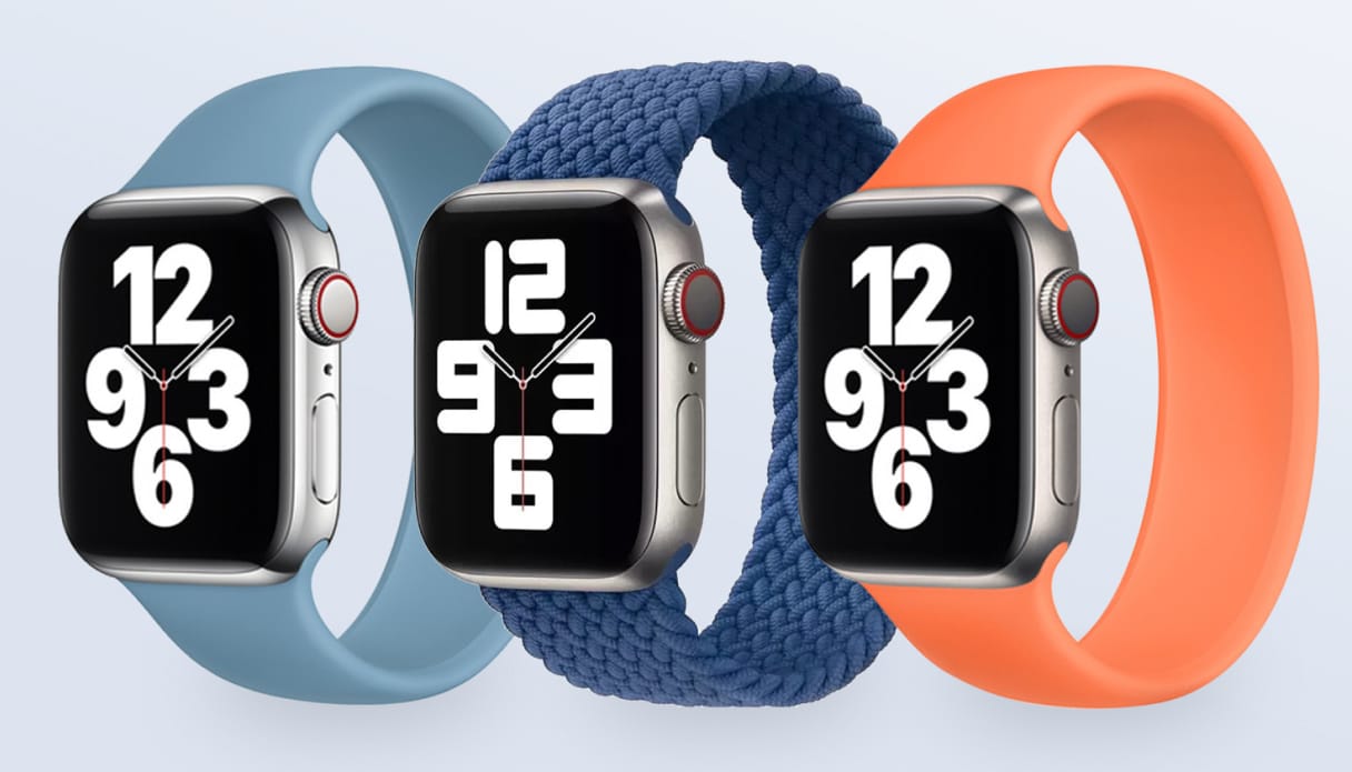 Drie Apple Watches met verschillende Apple Watch solobandjes op een lichtblauwe achtergrond. De solobandjes zijn van links naar rechts: northern blue siliconen solobandje, donkerblauw geweven solobandje, kumquat siliconen solobandje.
