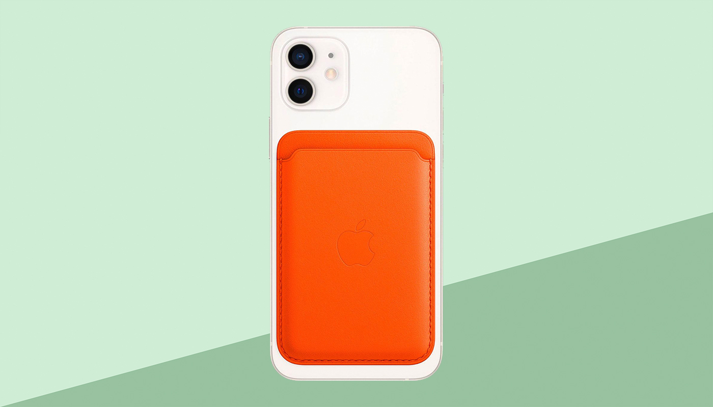 Een witte iPhone met oranje MagSafe leather wallet, de achtergrond is groen.