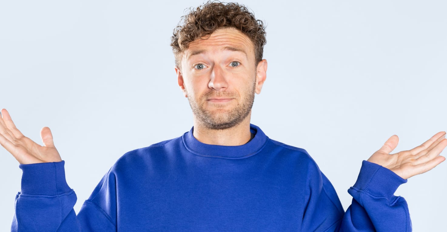 Een man in een blauwe trui steekt vragend zijn handen in de lucht.