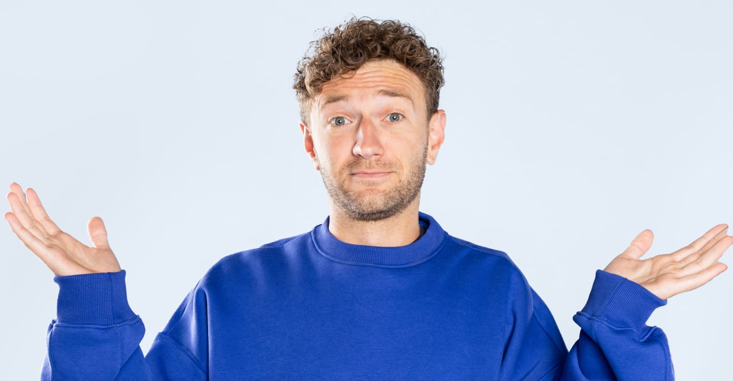 Een jongeman met een lichte huidskleur en donkerblond krullend haar heeft een vragend gezicht en houdt zijn handen vragend in de lucht. Zijn trui is blauw en de achtergrond lichtblauw.