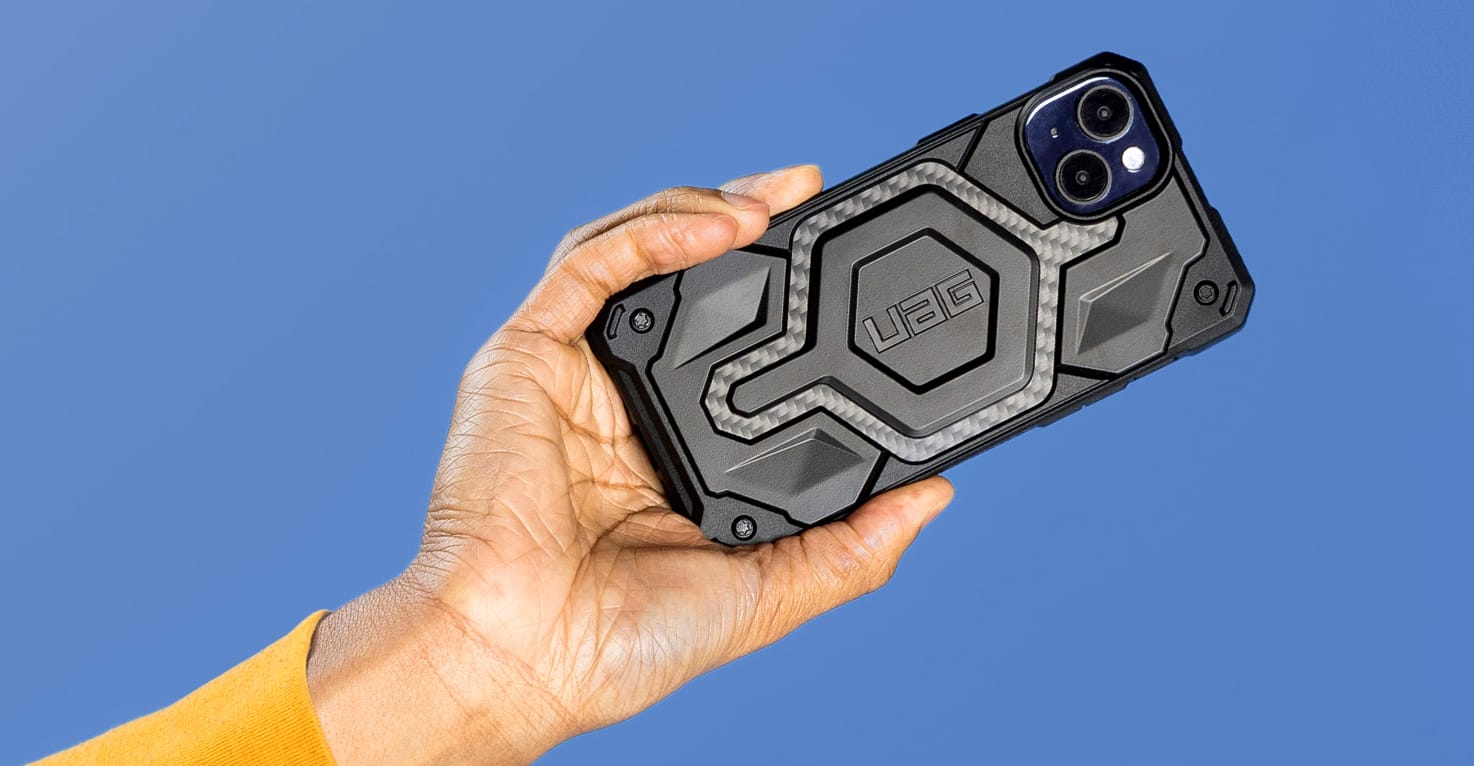 Een hand houdt een telefoon met een zwart UAG hoesje vast.