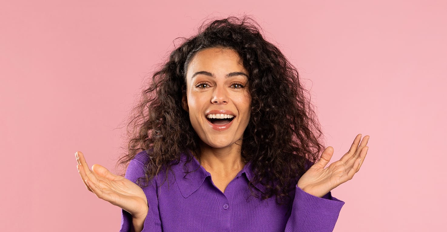 Een vrouw op een roze achtergrond die vragend haar handen in de lucht heeft.