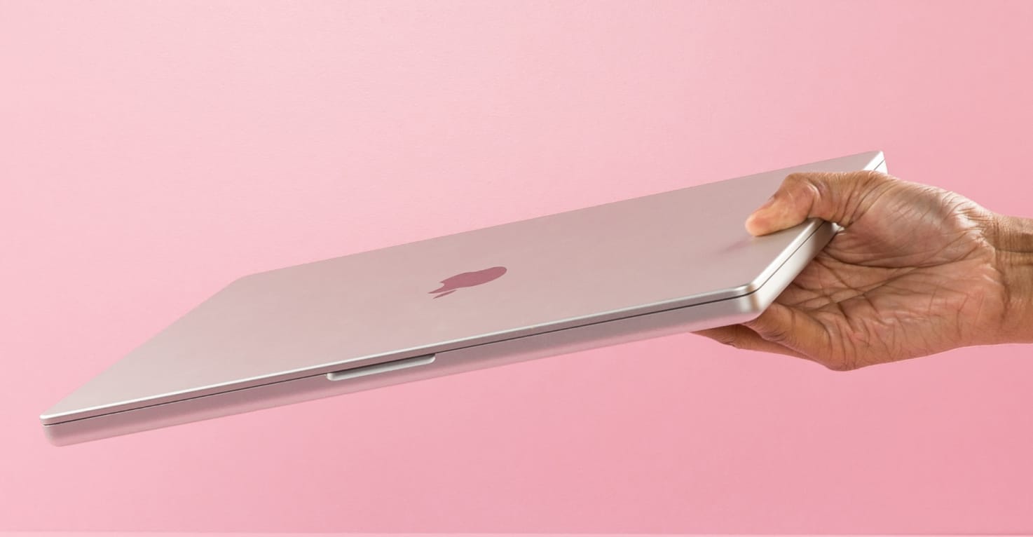 Een hand komt van rechts en heeft een MacBook vast.