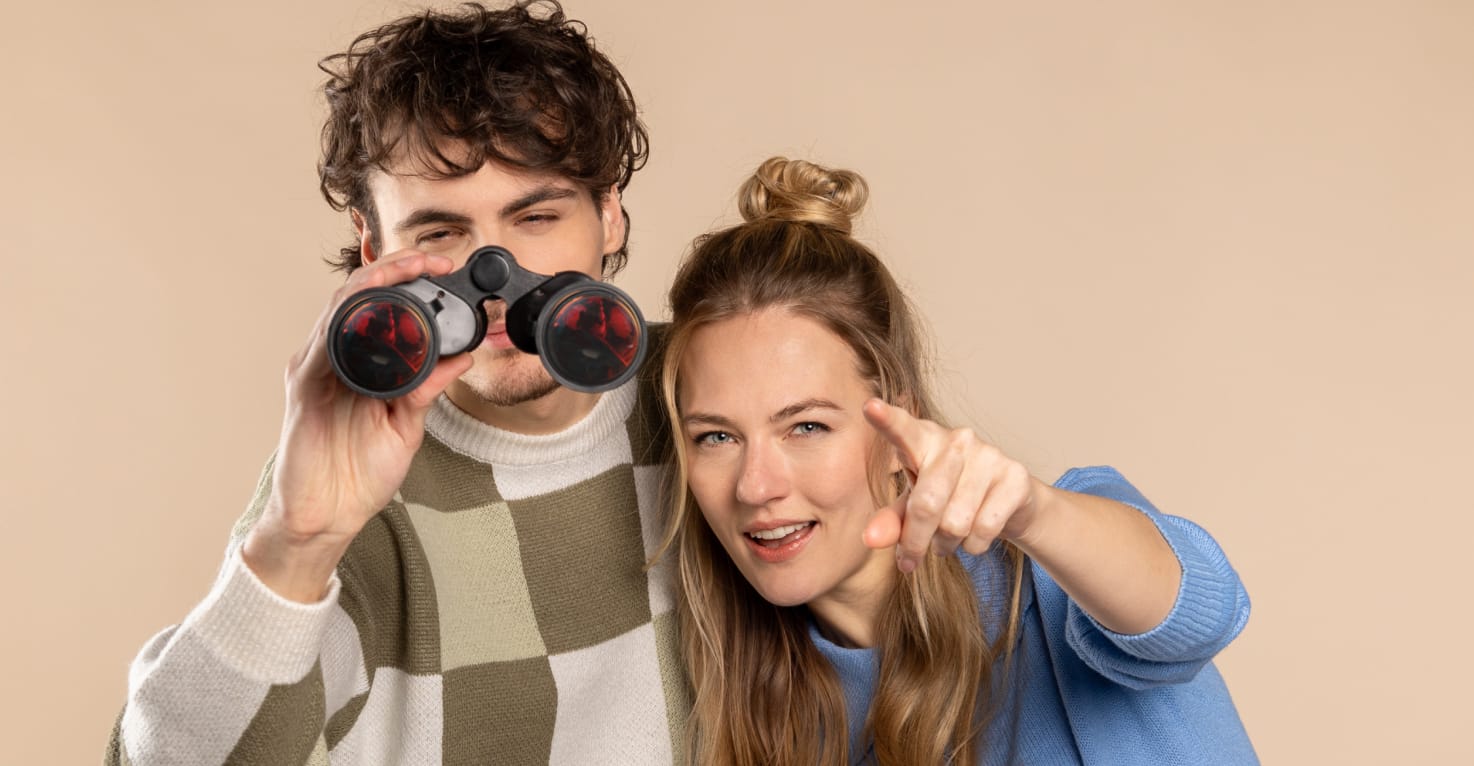 Een man met een verrekijker en een vrouw die in de verte wijst.