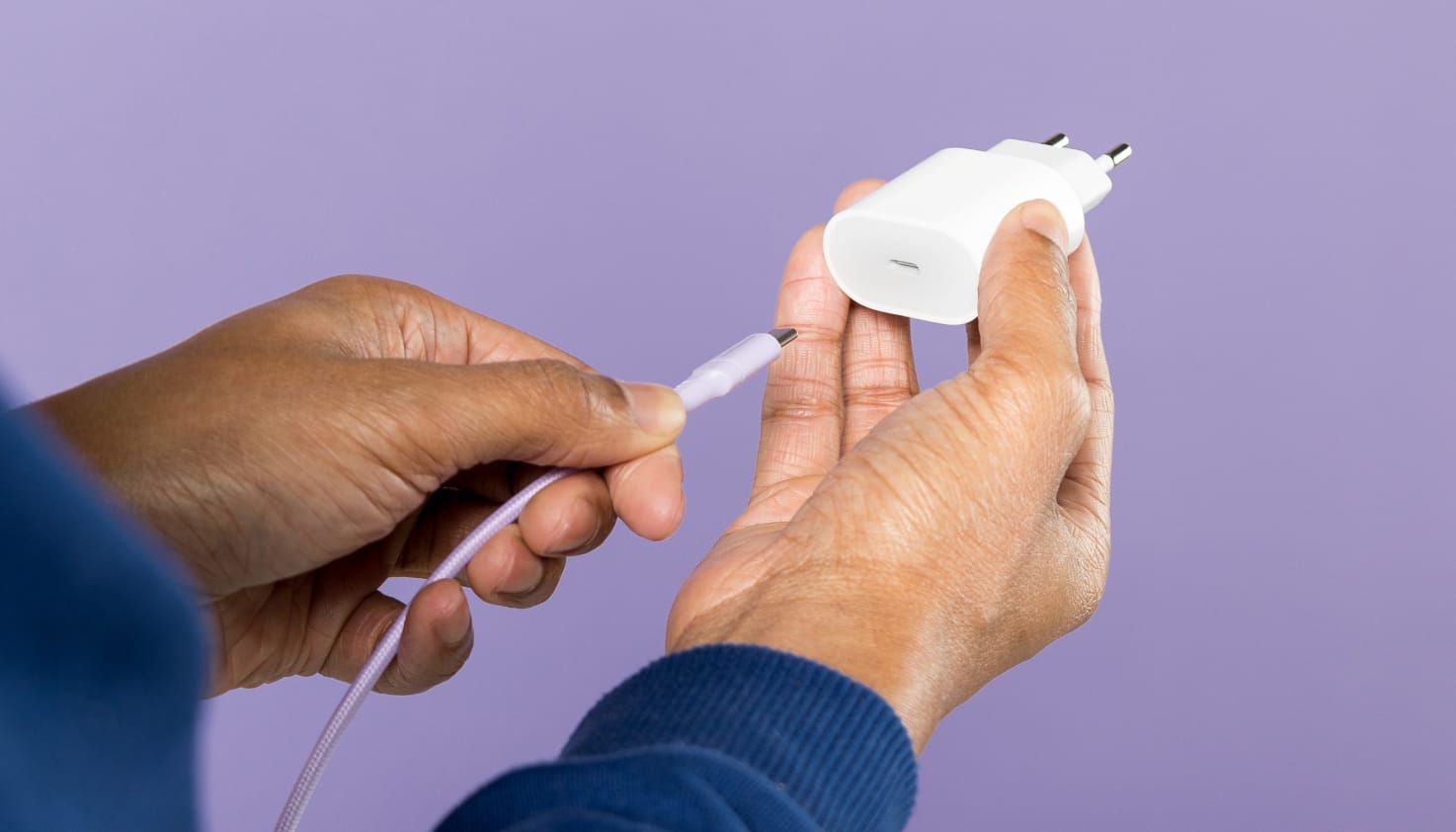 Een hand die een USB-C oplaadkabel in een adapter steekt.