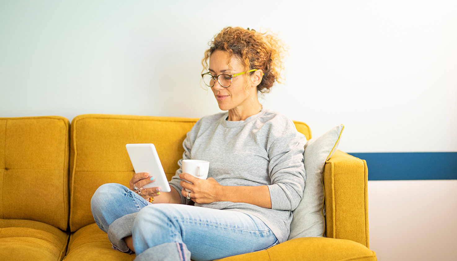 Een vrouw op de bank leest op een e-reader met een kop thee.