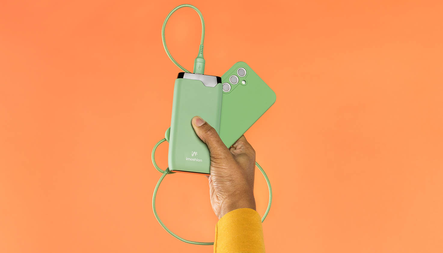 Groene powerbank die via een groene kabel verbonden is aan telefoon op een oranje achtergrond.